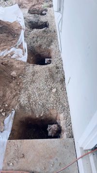 A line of pier holes opened along the base of the back wall, brackets set and gravel spread between them.