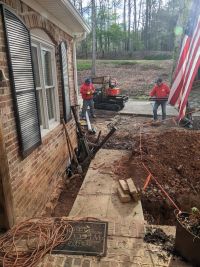 The wider front of the house, a tracked dumper on the drive and pier tubes laid along the walk beside the open excavation.