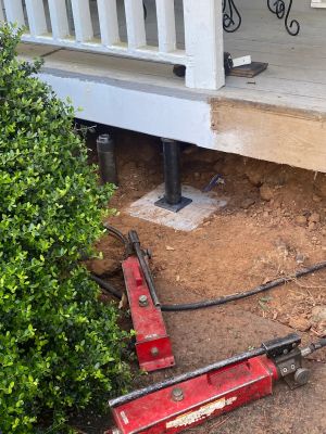 The same porch from the side, the pier and its footing in place and two hydraulic jacks resting on the ground.