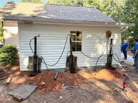 Three hydraulic rams braced against the side of the outbuilding, driving steel piers beside the slab.