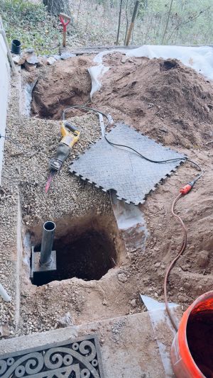 A pier tube standing in its hole with the bracket in place, the wooded slope rising behind the house.