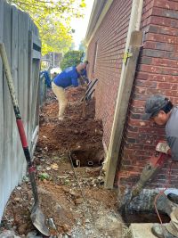 Anglin's crew opening a line of pier holes along the side of the house, one breaking concrete at the corner.