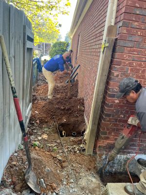 Anglin's crew opening a line of pier holes along the side of the house, one breaking concrete at the corner.