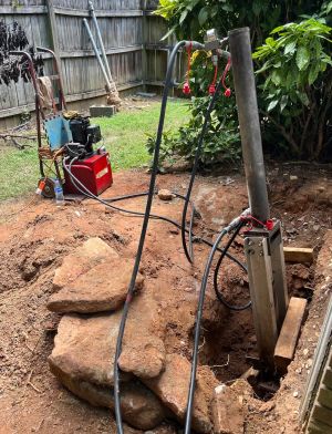 The pump and hoses set up in the yard, a pier ram working beside the large rock dug out of the hole.