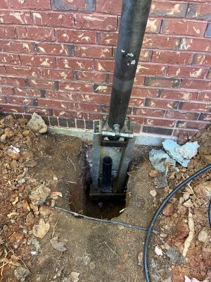 The pier bracket bolted under the footing, the pier tube running down into the ground.
