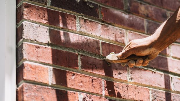 A mason's hand tooling a fresh mortar joint on a red brick wall