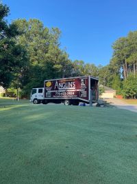 The Anglin's truck parked at the curb with its ramp down and a wheelbarrow alongside.