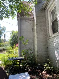 A full-height vertical crack where the painted brick foyer separates from the wall of the house.