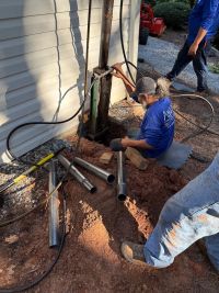 A crew member at the hydraulic controls beside an open pier hole, sections of steel pier tube on the ground.