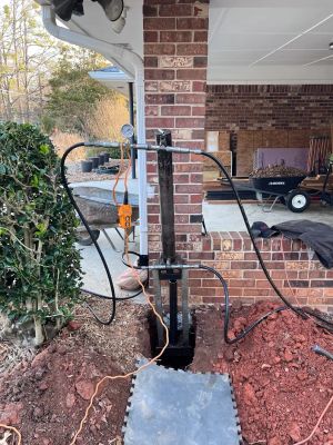 The hydraulic ram and pier bracket set in the open hole beside the brick carport column.