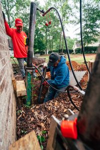An Anglin's crew member driving steel into Georgia clay beside a brick wall.