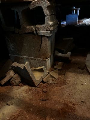 Before: the same block pier in the crawl space, broken pieces piled on the ground at its base.