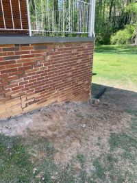 Stair-step cracking through the brick below the porch, with the ground along the footing turned over from the work.