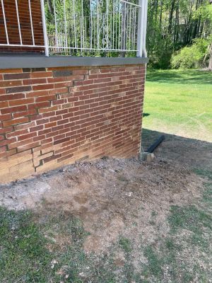 Stair-step cracking through the brick below the porch, with the ground along the footing turned over from the work.