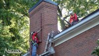 Anglin's crew members on a roof inspecting and working on a brick chimney.