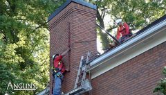 Anglin's crew members on a roof inspecting and working on a brick chimney.