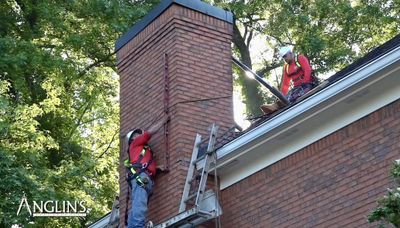 Anglin's crew members on a roof inspecting and working on a brick chimney.