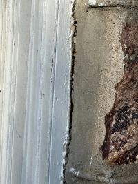 Close view of the gap opened between the painted trim and the masonry beside it.