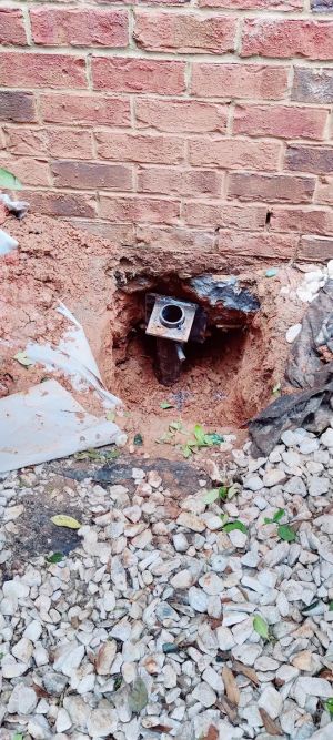The pier head and bracket seated in the excavation at the base of the brick wall, gravel backfilled around it.