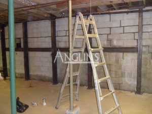 steel support beams in a basement of a bulding and with cracks between the bricks filled, there is a ladder in the foreground