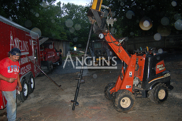 skid steer with a drill ready to dig into the ground and an anglin employee next to it