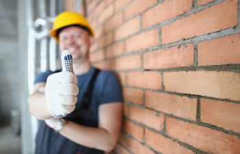 A professional masonry contractor leaning against a brick wall showing his thumb up.